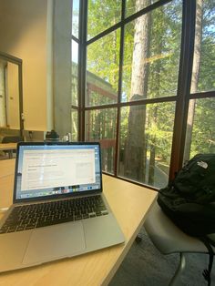 an open laptop computer sitting on top of a wooden desk in front of a window