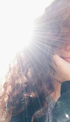 a close up of a person holding their hand to her face with the sun shining behind them