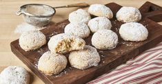 powdered sugar covered donuts on a wooden cutting board