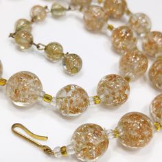 *Description: This is a beautiful clear Murano Italian glass beaded necklace made in the 1930s and filled with flecks of copper & gold which looks like glitter. Gold and copper within the beads is referred to as Aventurine. The necklace was designed with 20 12mm beads separated by clear and gold seed beads. There are six 8mm beads which are wire wrapped to add a matching extension chain. These are gorgeous Venetian beads and as a bead collector, these are one of my favorites. It is a beautif Vintage Murano Glass Beaded Necklace With Large Beads, Vintage Murano Glass Necklace With Large Beads, Vintage Clear Glass Necklaces, Antique Round Glass Necklaces, Vintage Clear Round Bead Necklaces, Antique Round Glass Necklace, Vintage Clear Glass Necklace, Vintage Glass Necklaces For Formal Occasions, Vintage Round Clear Jewelry