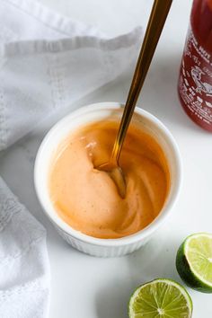 a small white bowl filled with sauce next to two limes