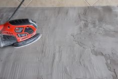 a cordless sanding machine is on the floor next to a tile pad with cement