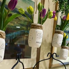 three mason jars with tulips tied to them are hung on a wall in front of a mirror