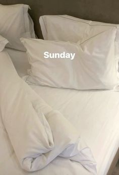 an unmade bed with white pillows and the word sunday written on it in cursive font