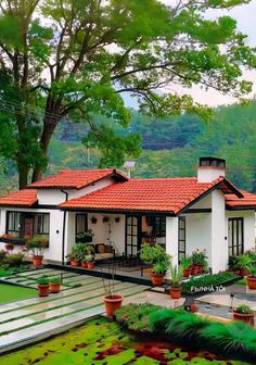 a white house with red tile roof and green plants in the front yard, surrounded by trees