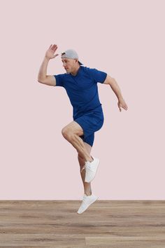 a man jumping in the air while wearing a blue shirt and white tennis shoes,