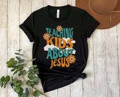 a t - shirt that says teaching kids about jesus on it next to a hat