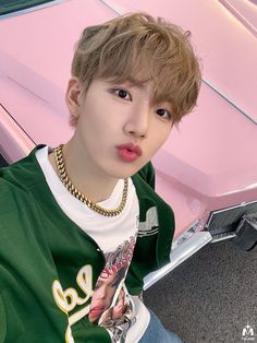 a young man sitting in front of a pink car wearing a green shirt and gold chain necklace