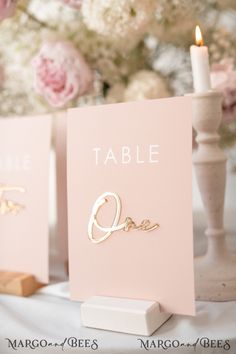 two cards with the word table written on them are next to a candle and some flowers