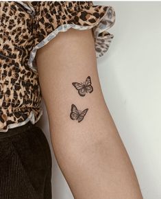 two butterflies tattoo on the left arm and right arm, with one butterfly in black ink