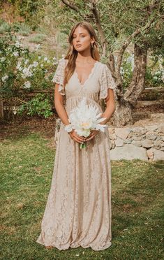 a woman in a long dress holding a white bouquet and posing for the camera with her hands on her hips