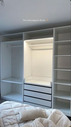 an empty white closet is shown with shelves and drawers on the wall, while a bed sits in front of it