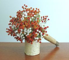 an arrangement of flowers in a vase on a wooden table with a cork handle and white wall behind it