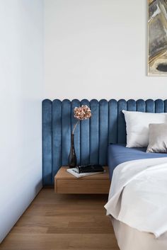 a bedroom with a blue headboard and white sheets on the bed, next to a painting