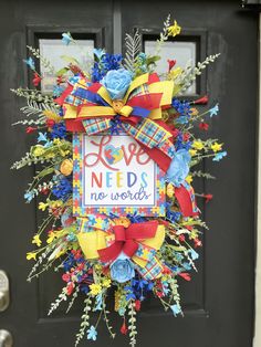 a colorful wreath with the words love needs no words is hanging on a black door