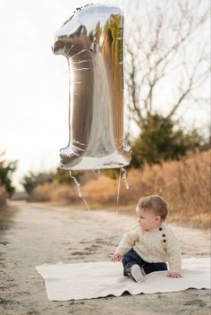 a little boy sitting on top of a white blanket next to a silver foil balloon