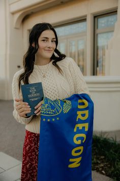 a woman holding a blue bag and a passport in front of a building with the word oregon written on it