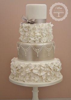 a three tiered wedding cake with white flowers on the bottom and silver ribbon around the top