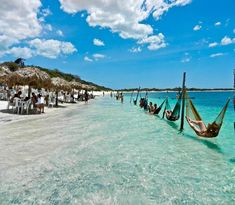 several hammocks are tied to poles on the beach as people walk in the water