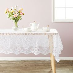 a white table with flowers and teapots on it in front of a window