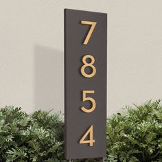 a black and gold house number sign next to bushes