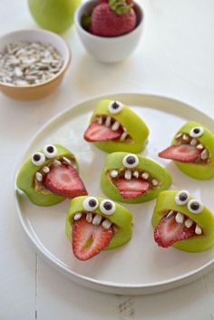 some strawberries with googly eyes on them are sitting on a white plate next to green apples