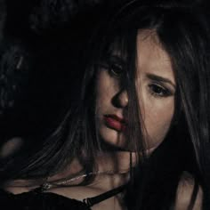 a woman with long dark hair and red lipstick looking down at the camera while wearing a choker