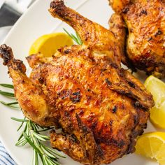 two pieces of chicken on a plate with lemons and rosemary