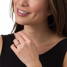 a woman wearing a diamond ring and black dress smiling at the camera with her hand on her chest