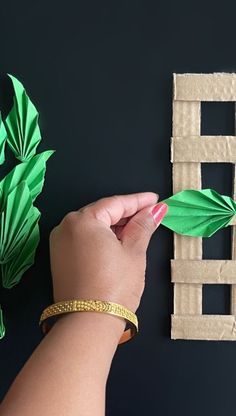 a person is cutting out some paper leaves on a black surface with a green plant in the background