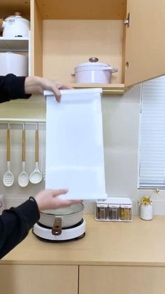 a woman holding up a piece of white paper in the kitchen with pots and pans behind her