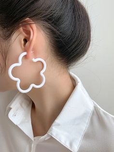 a close up of a person wearing large white earring with a flower design on it