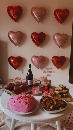 a table topped with lots of heart shaped balloons next to a cake and wine bottle