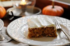 a piece of carrot cake on a plate with a fork and candle in the background