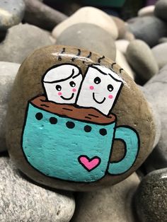 two marshmallows sitting in a mug on top of some rocks with hearts