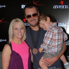 a man and woman holding a child in front of a wall with an advertisement on it