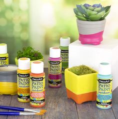 Bottles of DecoArt Patio Paint outdoor acrylic paint are placed in front of several flower planters painted in colorful stripes Americana Decor, Paint Supplies, Craft Store, Neon Color