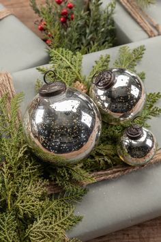 three silver ornaments sitting on top of a table next to evergreen branches and red berries