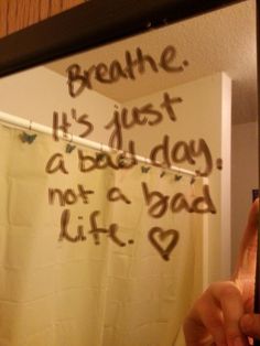 a person taking a selfie in front of a bathroom mirror with writing on it