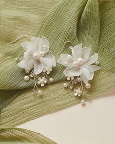 two white flowers and pearls are on a green leafy piece of cloth with beads