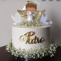 a white cake with gold lettering and an angel on top, surrounded by baby's breath flowers