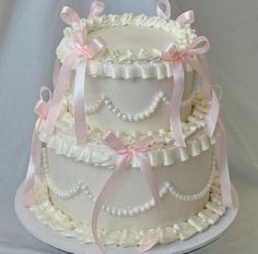 a three tiered wedding cake with pink bows and pearls on the top, sitting on a white platter