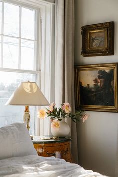 a bed with white sheets and flowers in a vase next to a lamp on a table