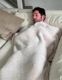 a man laying on top of a white couch under a blanket