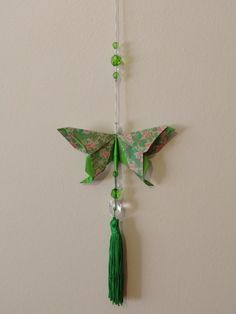 an origami butterfly hanging from a string with beads and green tassels