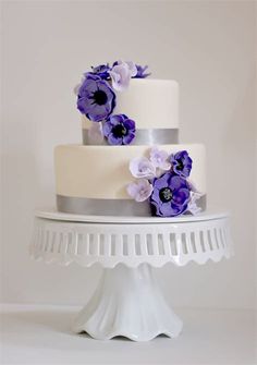 a three tiered cake with purple flowers on the top and silver trimmings