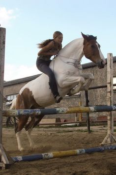 a woman riding on the back of a brown and white horse over an obstacle course