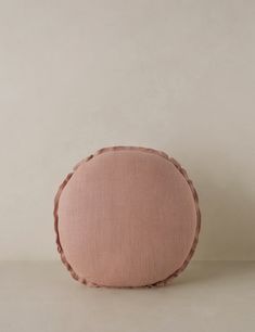 a pink pillow with braiding on the side and a white wall in the background