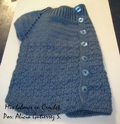 a blue knitted sweater with buttons on the front and back, sitting on top of a table