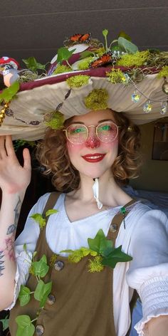 a woman wearing a large hat with flowers on it's head and green leaves around her neck